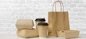 Fast food packaging set. Paper coffee cups, food boxes, brown paper bag on the table on white brick wall background