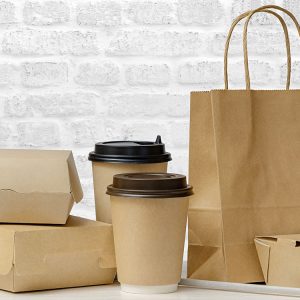 Fast food packaging set. Paper coffee cups, food boxes, brown paper bag on the table on white brick wall background